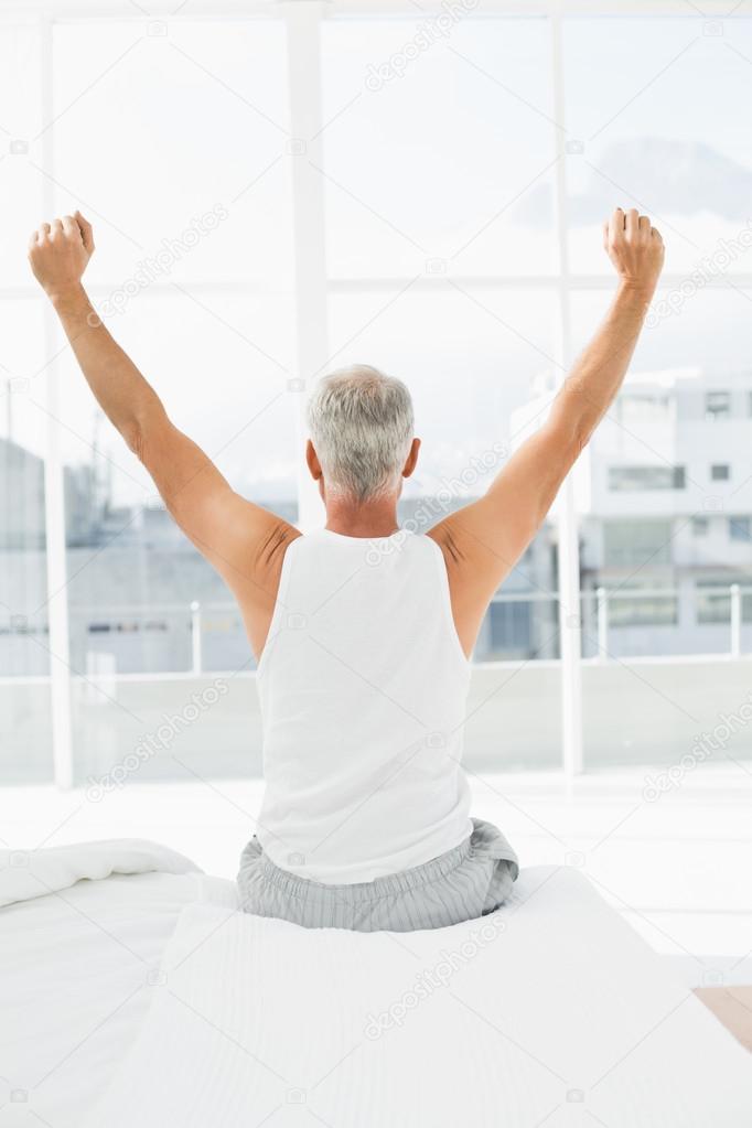 Rear view of mature man stretching arms in bed