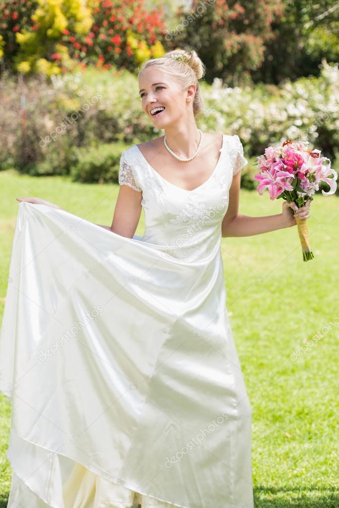 Pretty blonde bride holding bouquet and her dress