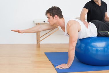 Fiziksel terapist yardımcı yoga topu ile genç adam