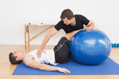 Fiziksel terapist yardımcı yoga topu ile genç adam