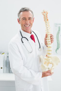 doktor ofisinde iskelet modeli tutan gülümseyerek