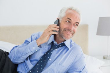 iyi giyimli adam cep telefonuyla yatakta rahat