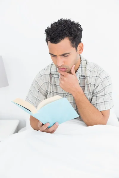 Ernsthafter junger Mann liest Buch im Bett — Stockfoto