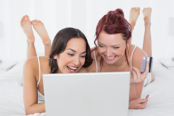 Avslappnad kvinnliga vänner gör online shopping i sängen — Stockfoto