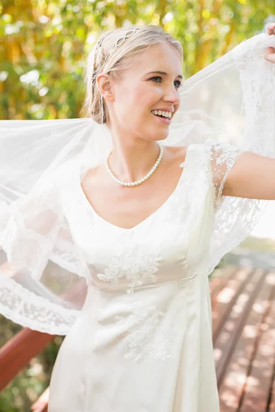 Pretty smiling blonde bride holding her veil out — Stock Photo, Image