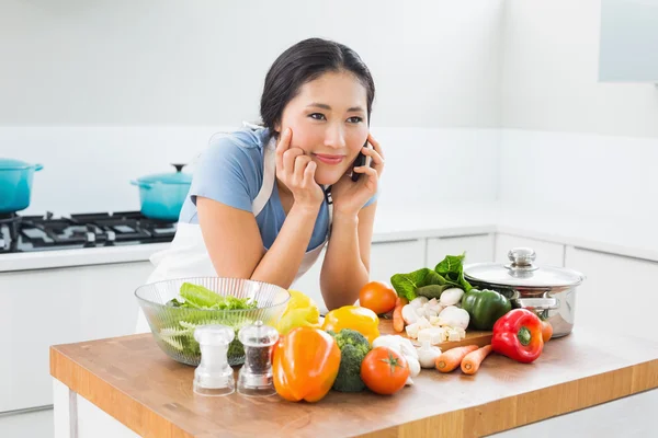 Vrouw met behulp van mobiele telefoon vóór groenten in de keuken — Stockfoto