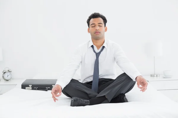 Relaxed businessman sitting in lotus pose on bed — Stock Photo, Image