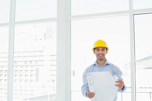 Smiling architect in yellow hard hat with blueprint in office — Stock Photo, Image