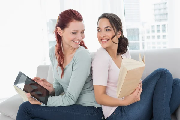 Unga kvinnliga vänner med digital tablet och bok hemma — Stockfoto