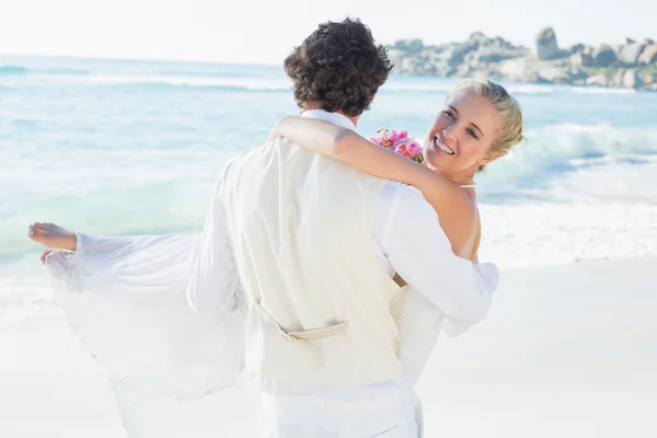 Schöner Bräutigam trägt seine schöne Frau lächelnd in die Kamera — Stockfoto