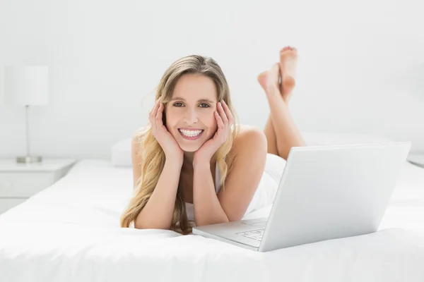 Sorrindo jovem mulher com laptop deitado na cama — Fotografia de Stock