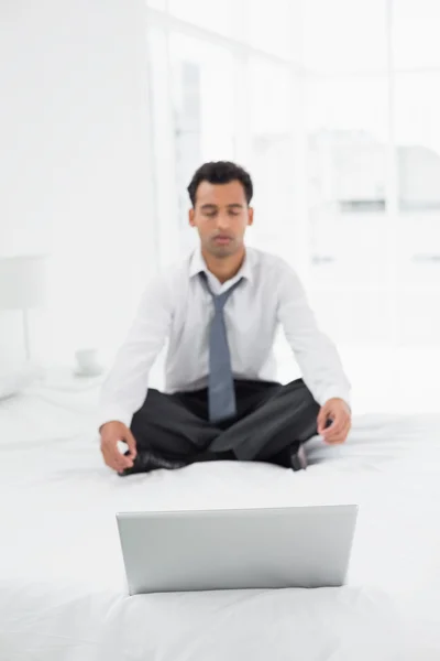 Zakenman die in lotus pose met laptop op bed zitten — Stockfoto