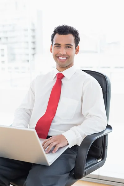 Улыбающийся бизнесмен с ноутбуком сидит в офисе — стоковое фото