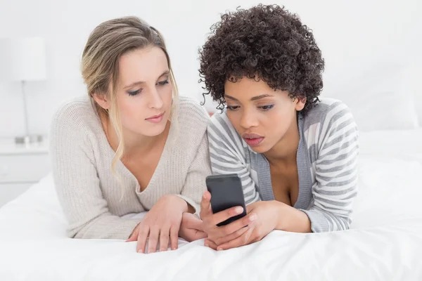 Serious female friends reading text message in bed — Stock Photo, Image