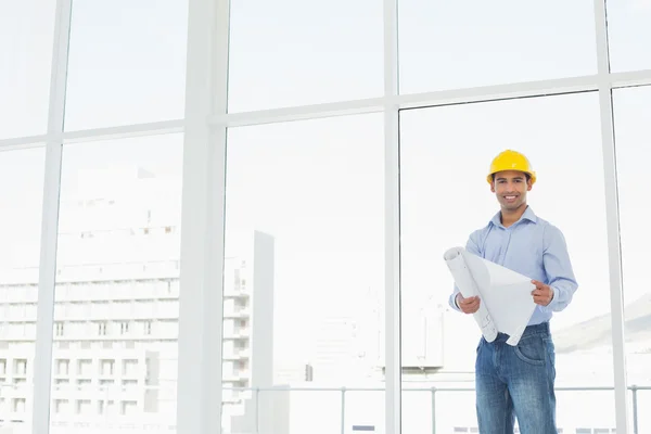 Young architect in yellow hard hat with blueprint in office — Stock Photo, Image