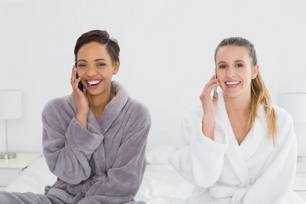 Vriendinnen in badjassen met behulp van telefoons op bed — Stockfoto