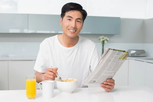 在厨房里看着报纸同时有谷物的男人微笑着 — 图库照片