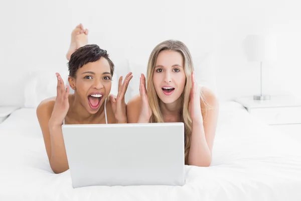 Geschokt jonge vrouwelijke vrienden met laptop in bed — Stockfoto