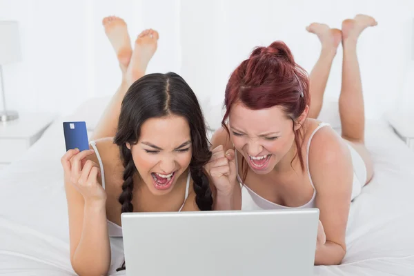 Cheerful female friends doing online shopping in bed — Stock Photo, Image