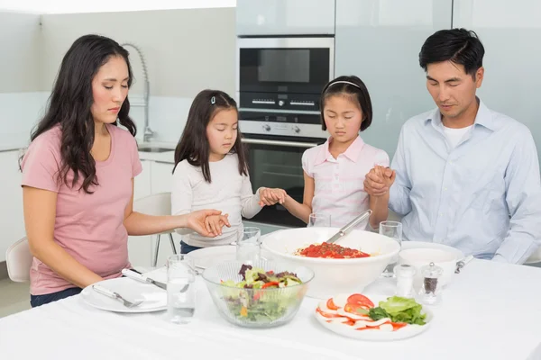 Familj på fyra säger grace före måltid i köket — Stockfoto