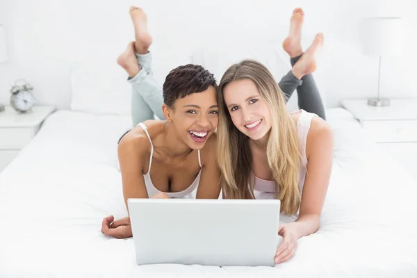 Felices amigas relajadas usando laptop en la cama —  Fotos de Stock