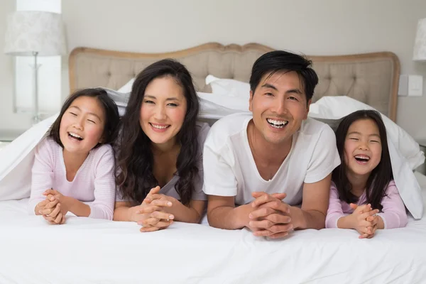 Porträt einer fröhlichen vierköpfigen Familie, die im Bett liegt — Stockfoto
