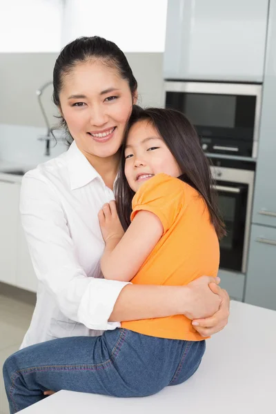 Porträt einer Mutter, die ihre kleine Tochter in der Küche trägt — Stockfoto