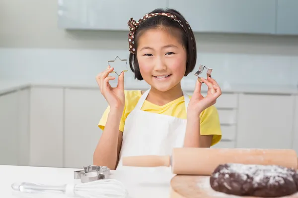 Smiling young girl holding cookie molds in kitchen — Stock Photo, Image
