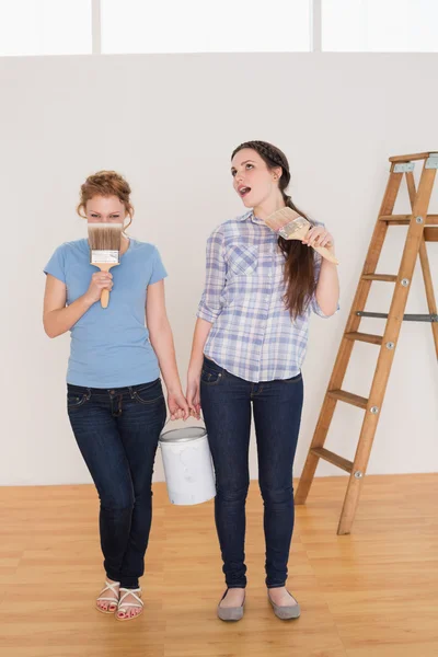 Amici che tengono pennelli e possono in una nuova casa — Foto Stock