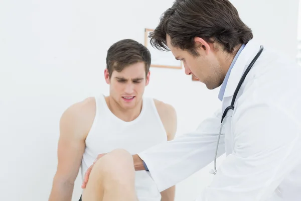 Displeased young man getting his leg examined — Stock Photo, Image