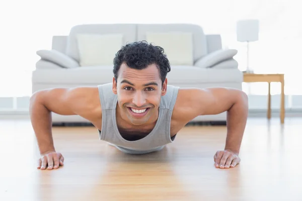Sporty smiling man doing push ups in the living room — Stock Photo, Image