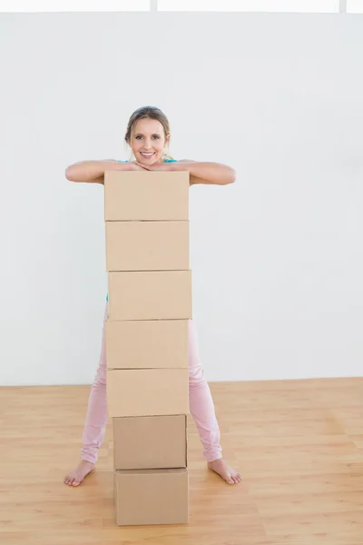 Mujer sonriente moviéndose en una casa nueva con una pila de cajas — Foto de Stock