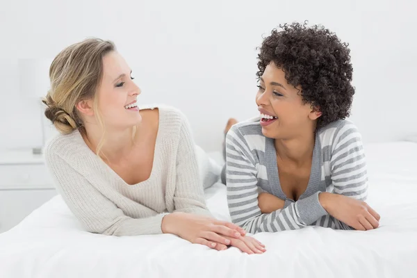 Deux amies souriantes et détendues couchées au lit — Photo