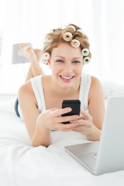 Kvinna i hår papiljotter textmeddelanden av laptop i sängen — Stockfoto