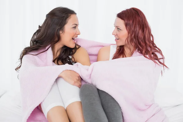 Female friends covered in sheet while chatting on bed — Stock Photo, Image