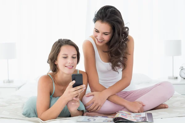 Mujeres amigas leyendo mensajes de texto en la cama —  Fotos de Stock