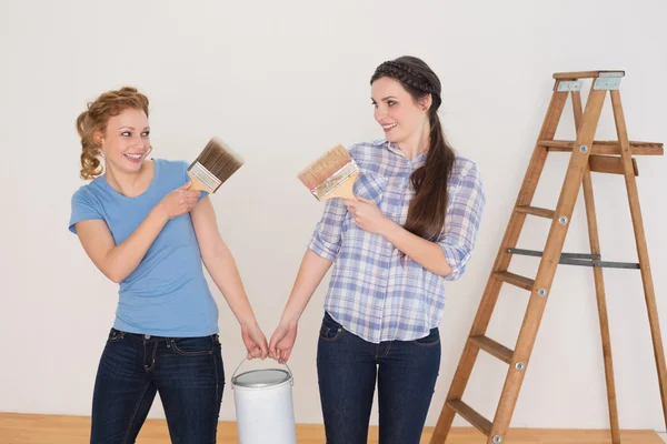 Friends holding paint brushes and can in a new house — Stock Photo, Image