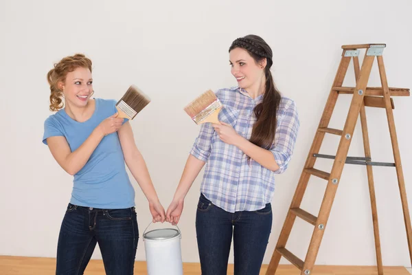 Amigos segurando pincéis e lata em uma nova casa — Fotografia de Stock