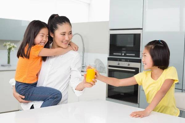 Girl offering her mother a glass of orange juice in kitchen — Stock Photo, Image