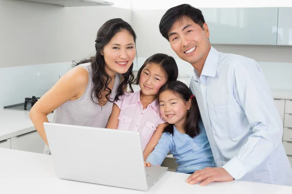 Retrato de una familia feliz de cuatro con portátil en la cocina —  Fotos de Stock