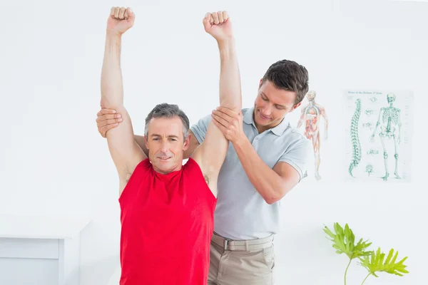 Sjukgymnast undersöka en leende mogen mans arm — Stockfoto