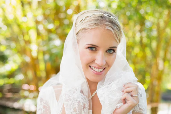 Beautiful blonde bride holding her veil smiling at camera — Stock Photo, Image