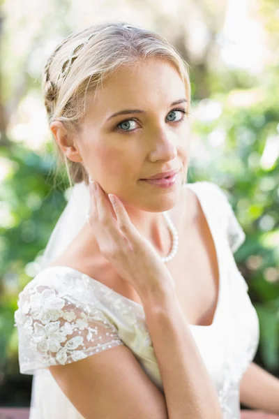 Улыбающаяся невеста-блондинка в жемчужном ожерелье касается ее лица — стоковое фото