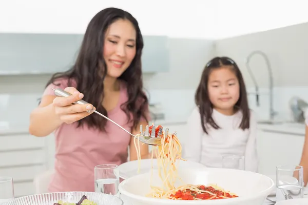 Klein meisje kijken gelukkig vrouw serve spaghetti in keuken — Stockfoto