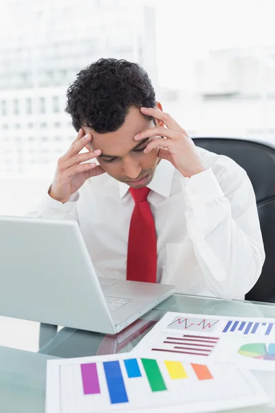 Hombre de negocios serio con portátil y gráficos en el escritorio —  Fotos de Stock