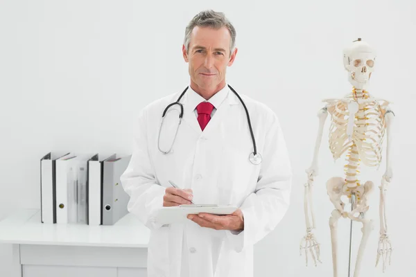 Médico varón sonriente escribiendo un informe en el consultorio —  Fotos de Stock