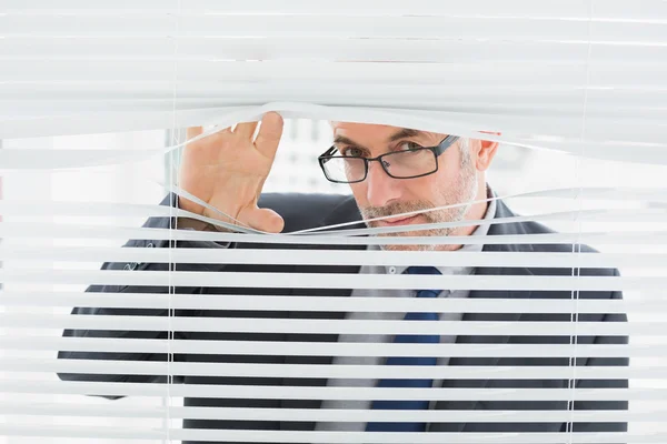 Primer plano de un hombre de negocios mirando a través de las persianas en la oficina — Foto de Stock