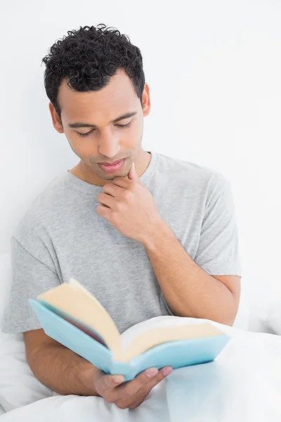 Serious relaxed man reading book in bed — Stock Photo, Image