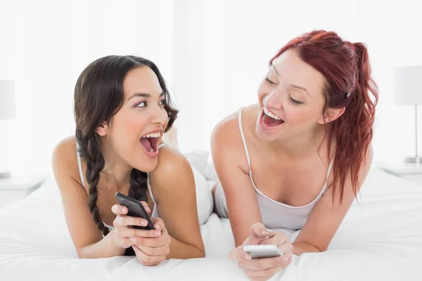 Glada unga kvinnliga vänner textmeddelanden på sängen — Stockfoto