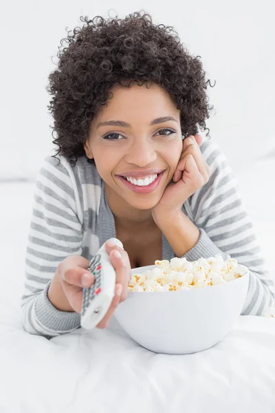 Lachende vrouw met afstandsbediening en popcorn kom in bed — Stockfoto